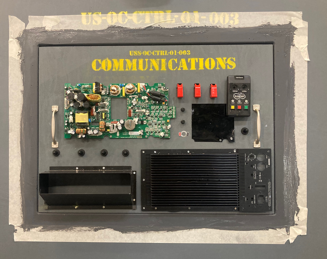 wooden panel with &quot;communications&quot; spray painted on, with a circuit board screwed in